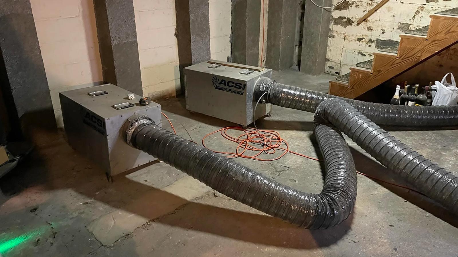 Two air movers connected to flexible ducts in a basement space.