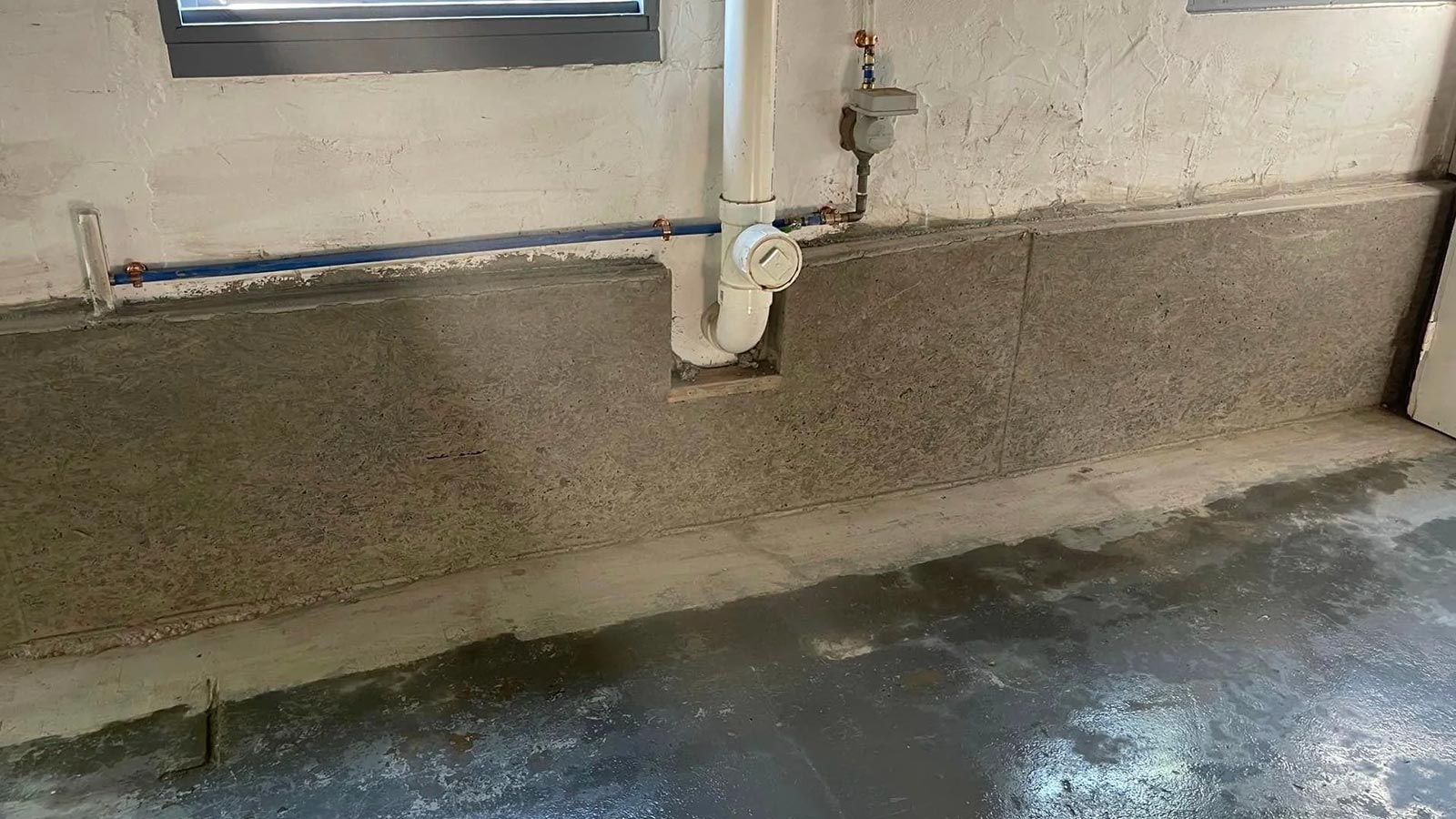 Basement wall with freshly poured concrete floor and plumbing pipe.