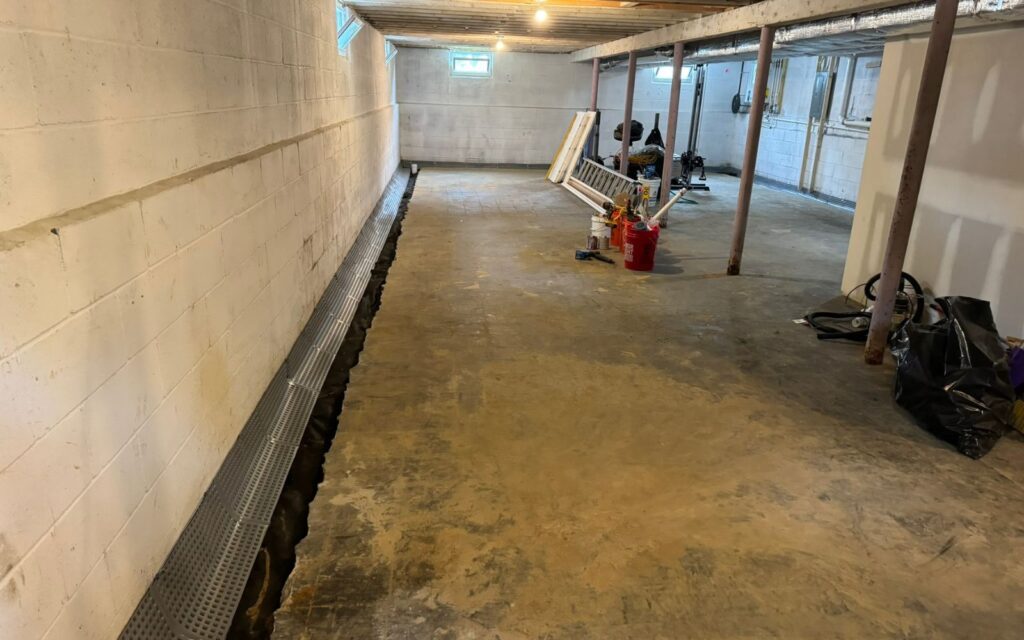Basement floor with a new drainage system installed along the wall.