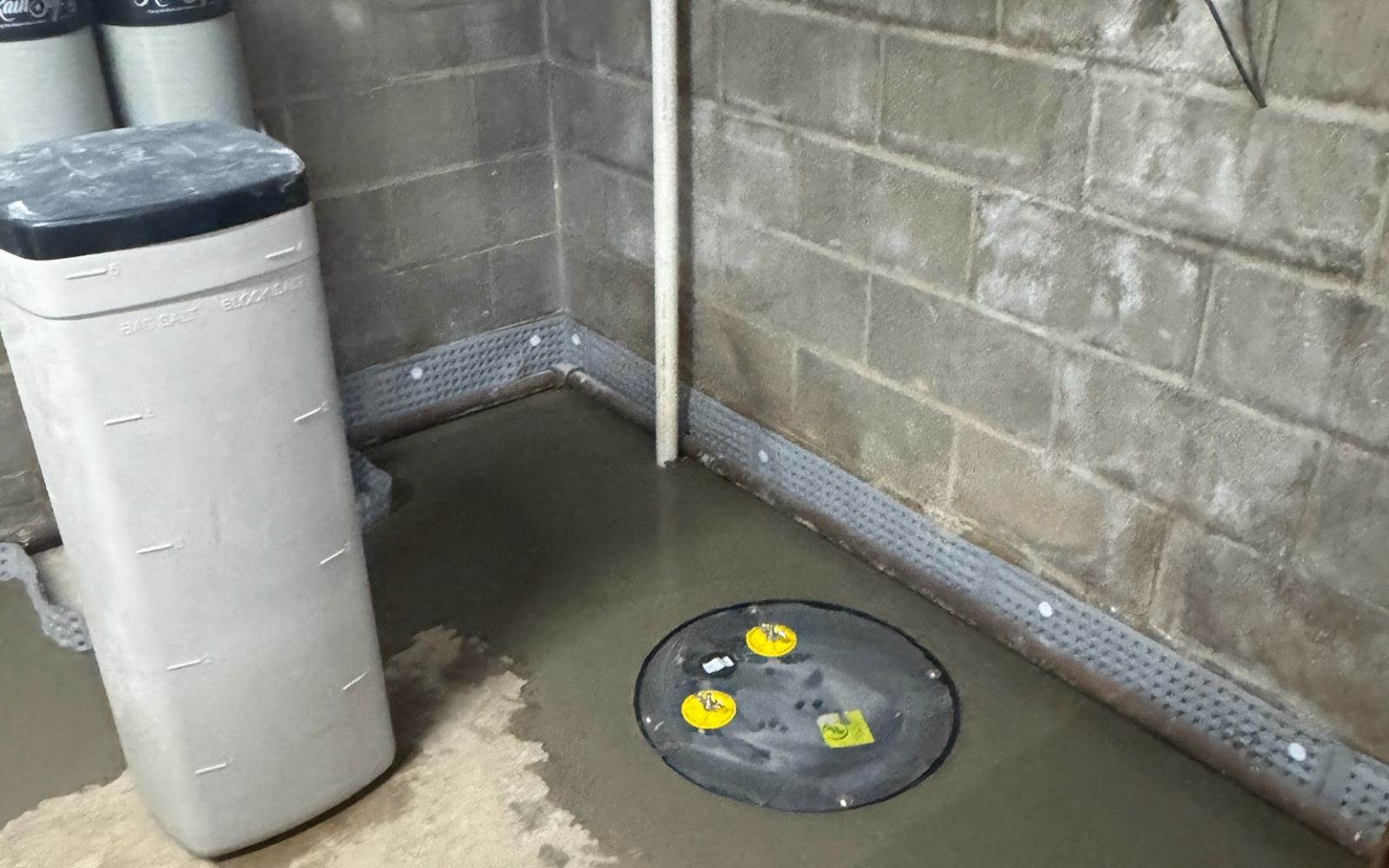 Basement sump pump installation with concrete floor and wall drainage system.
