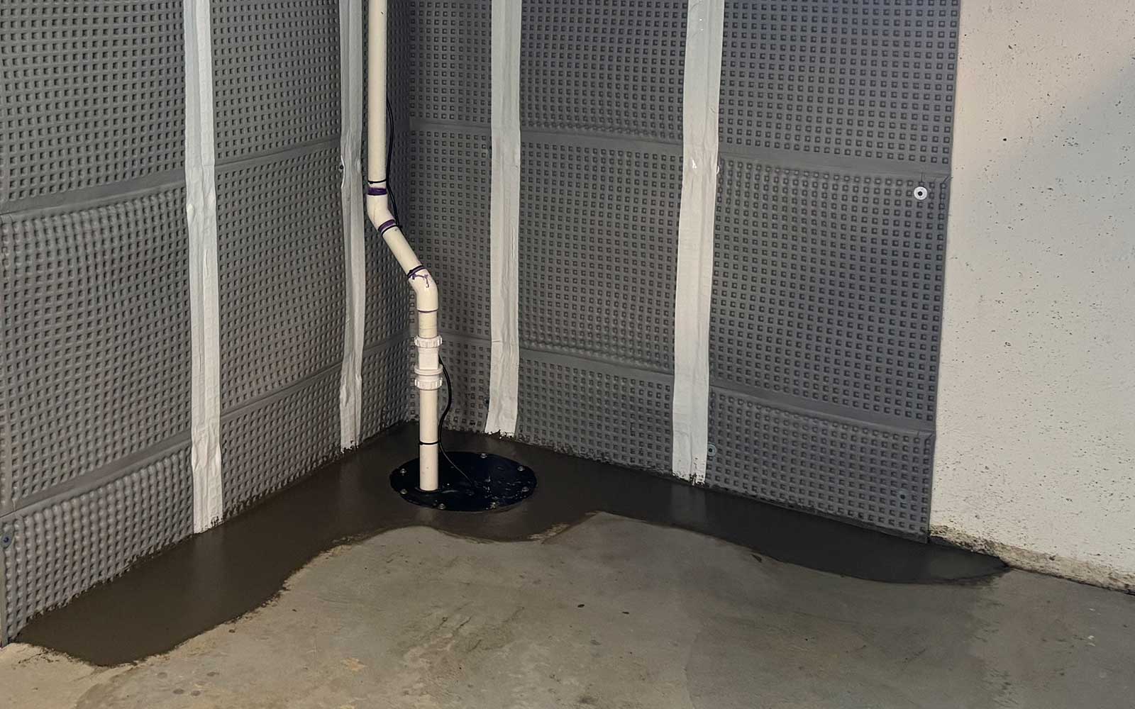Sump pump system installed in a basement corner with water accumulation on the floor.