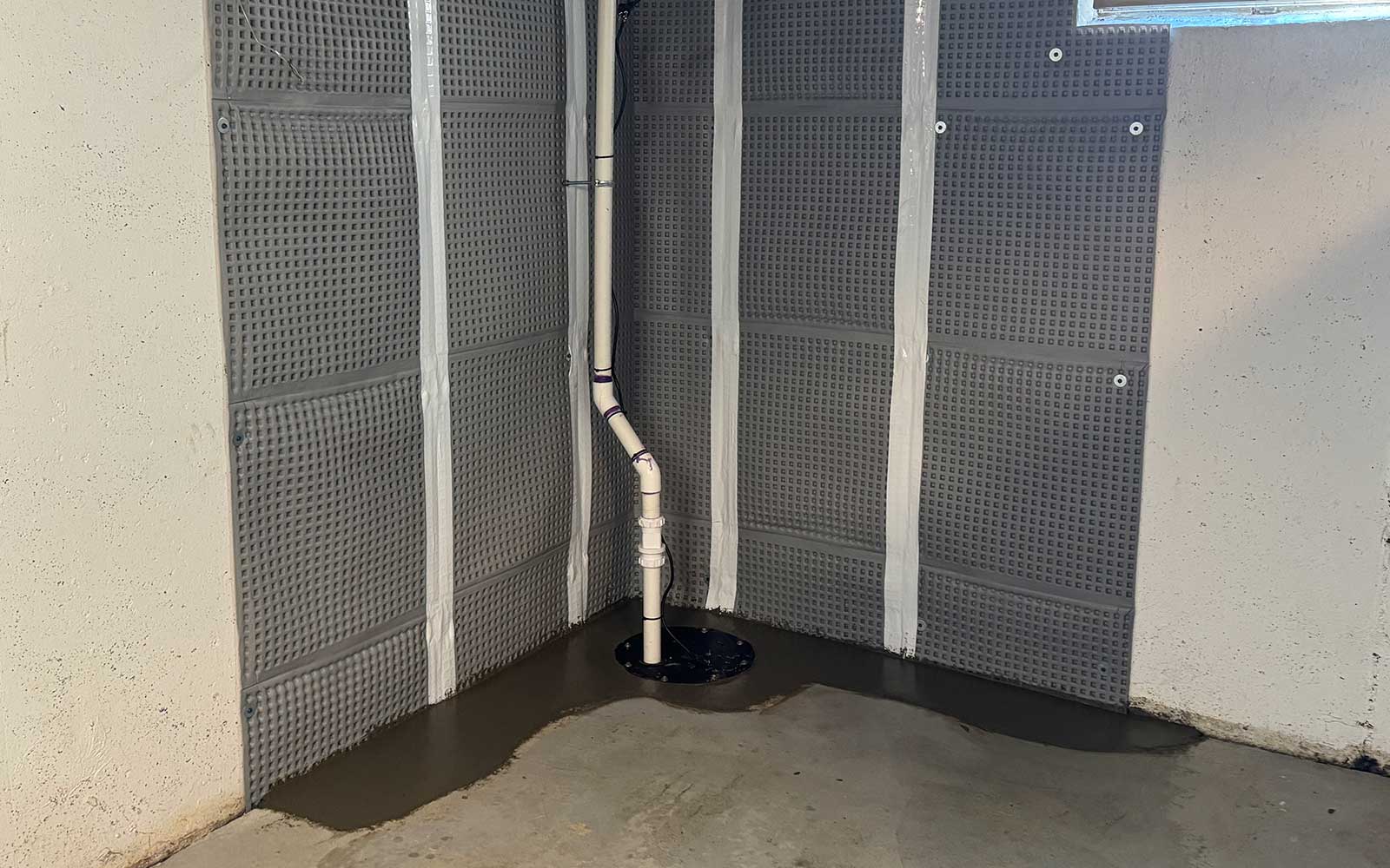 Sump pump system installed in a basement corner with water accumulation on the floor.