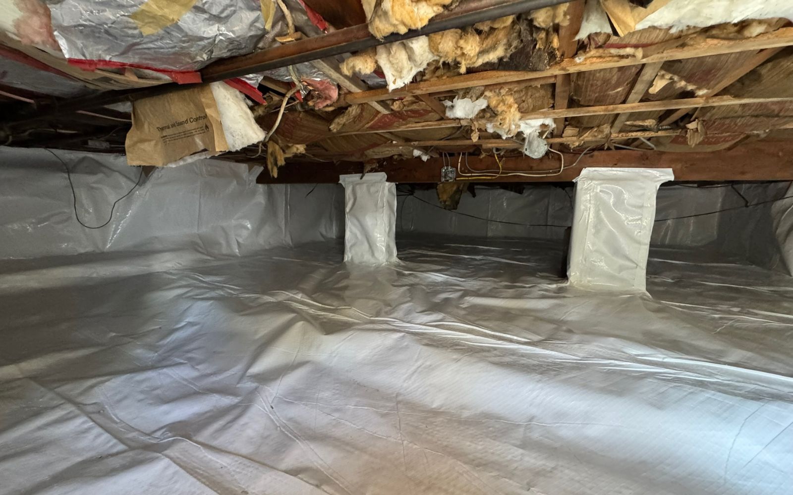 Crawl space with vapor barrier covering the floor and white encapsulation material on the walls.