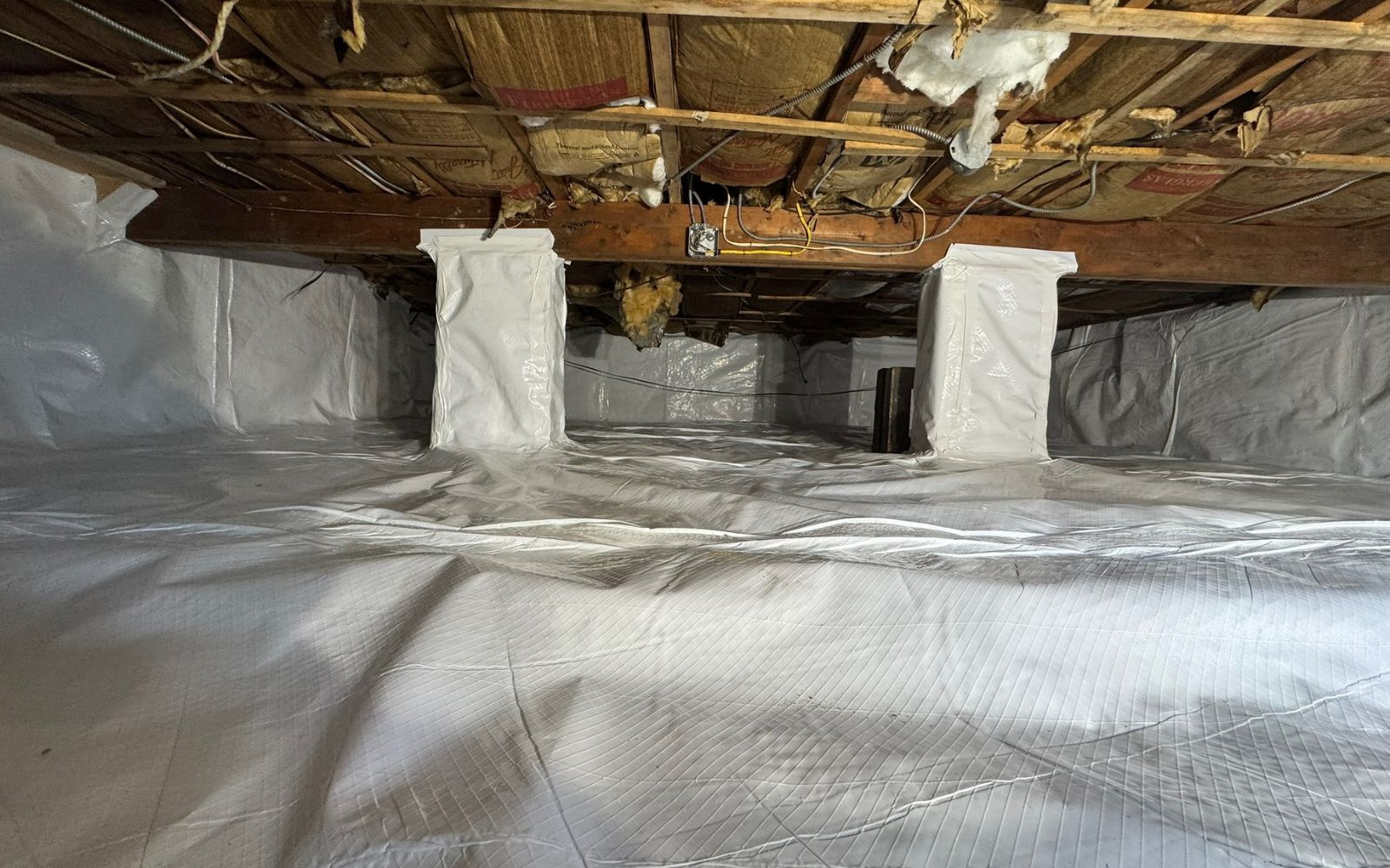 Crawl space with vapor barrier covering the floor and white encapsulation material on the walls.