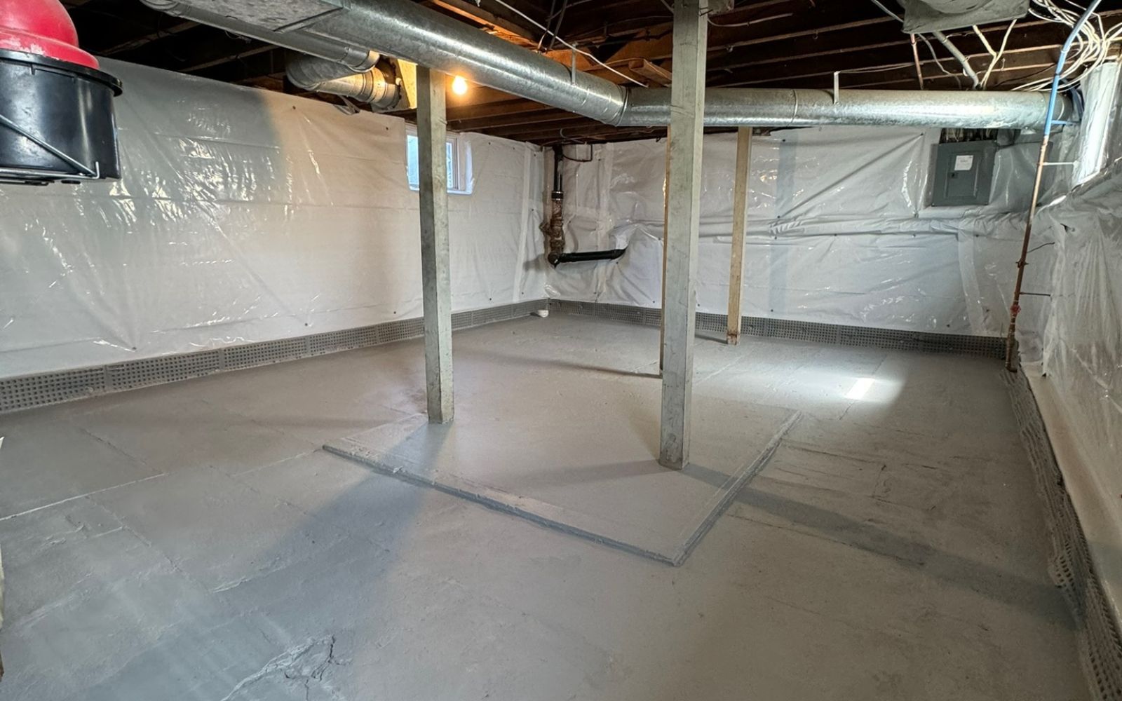Basement with concrete floor, vapor barrier installed, and exposed support beams.