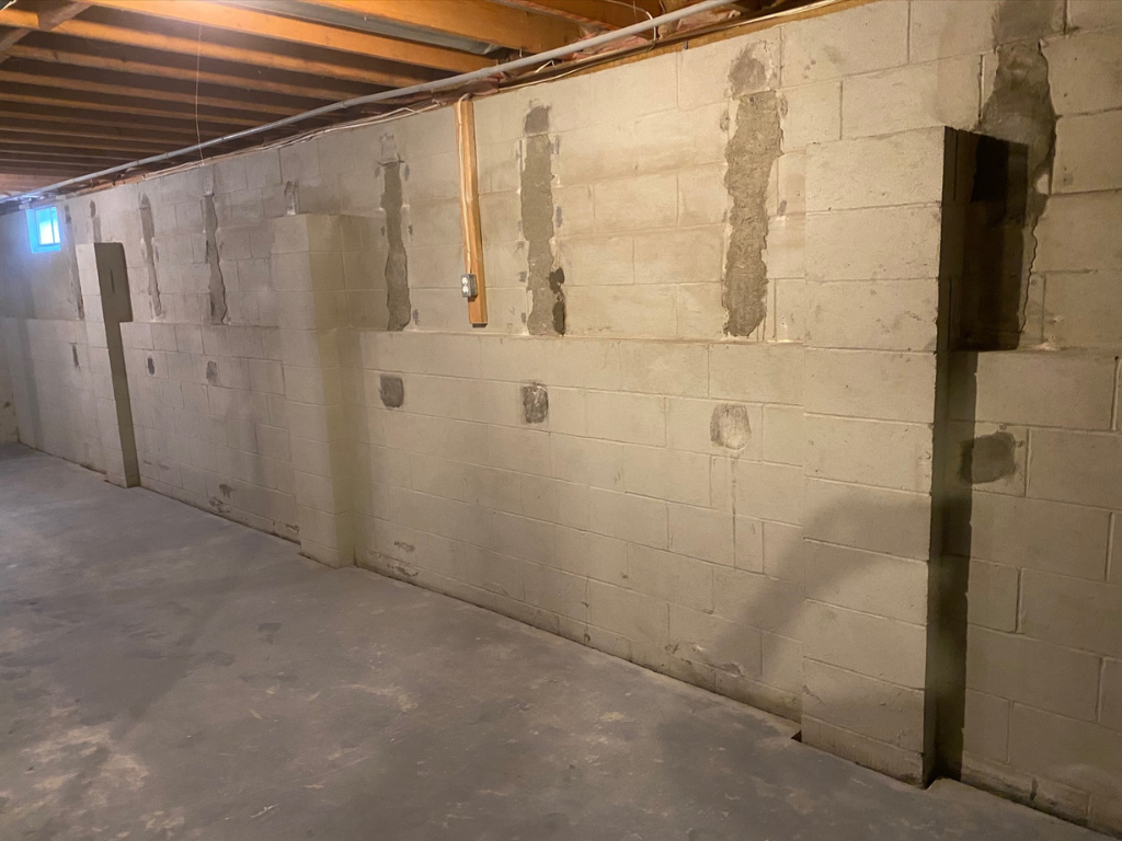 A basement wall under construction, with cinder blocks showing gaps and unfinished areas, indicating the progress of a foundation or basement repair project.