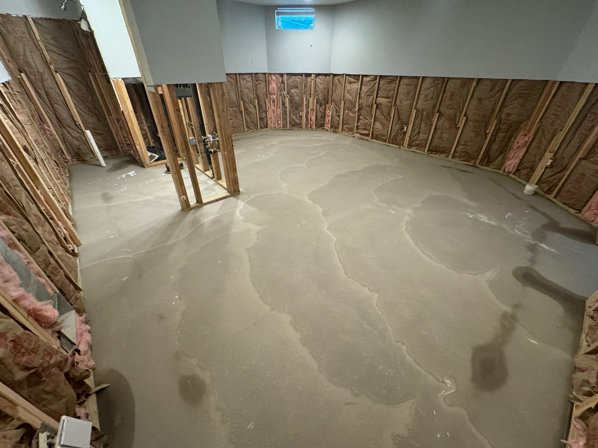 user-inserted Basement undergoing flood damage repair with exposed framing, insulation, and freshly leveled concrete floor, ready for further restoration work.
