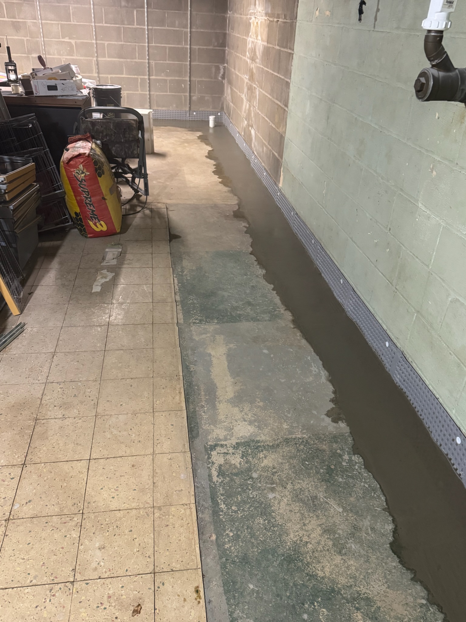 user-inserted Basement with installed drainage system showing water pooling along the floor, with a drainage perimeter system in place to manage water flow and prevent flooding.