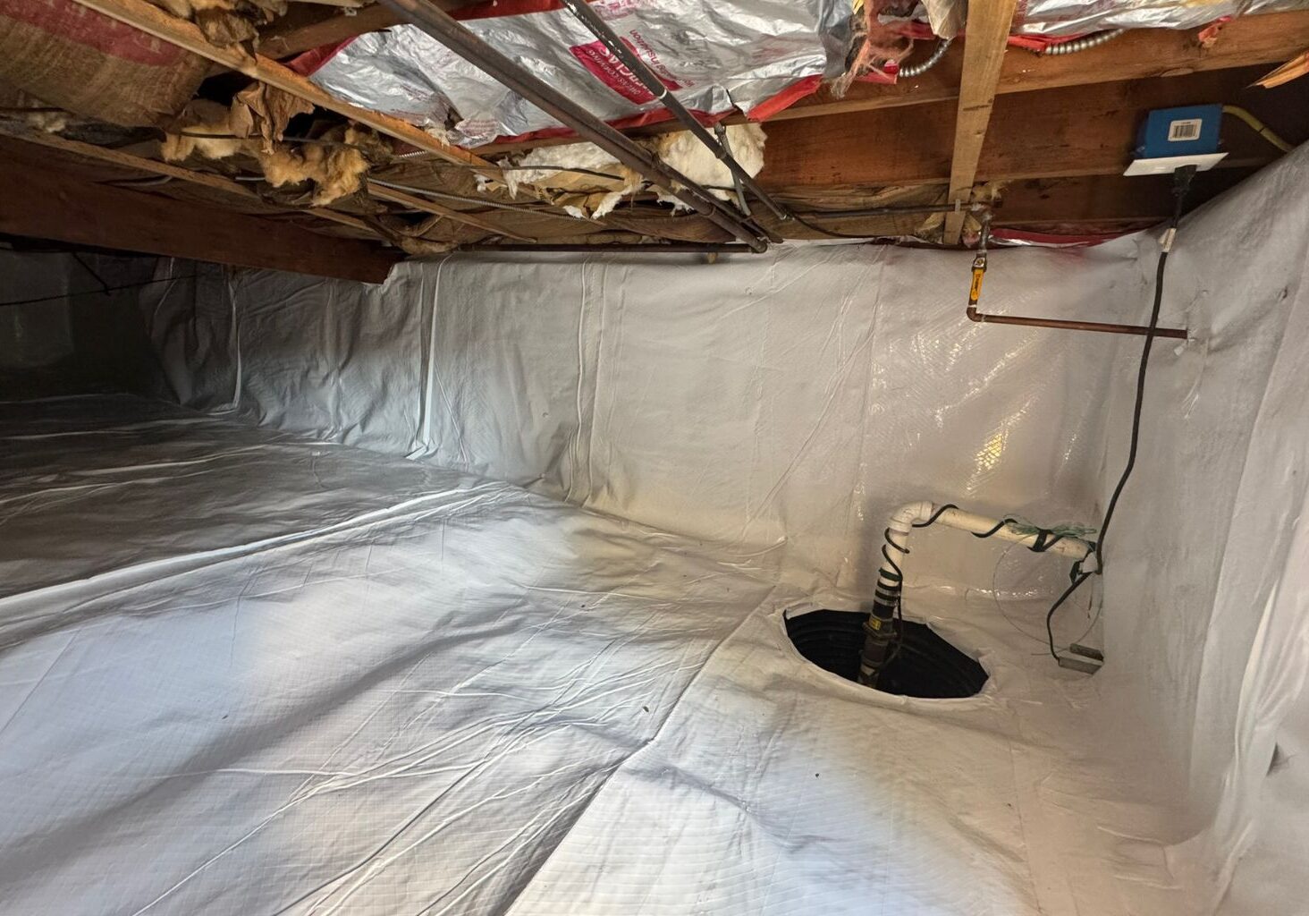 Installed vapor barrier in a crawl space with a sump pump, providing moisture control and protection against mold, water damage, and air quality issues. Learn how a sealed crawl space can improve your home's health and energy efficiency.