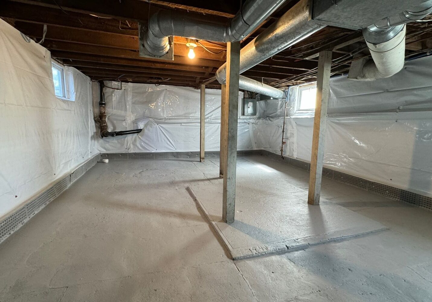 Basement with concrete floor, vapor barrier installed, and exposed support beams.